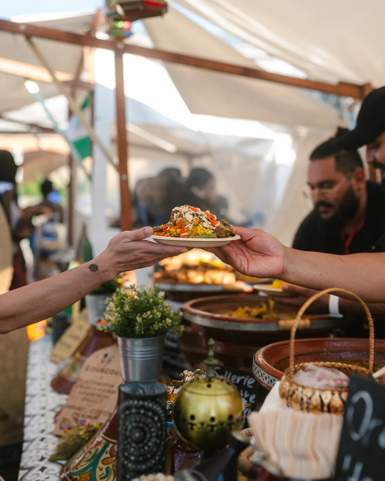 Ein Teller Couscous wird im Festivalzelt über die Theke gereicht, daneben Tajine-Töpfe und ein Messingbrenner
